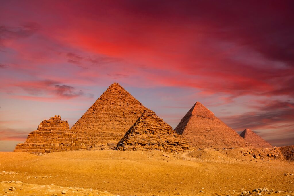 Three pyramids on the Giza Plateau beneath a red sunset sky