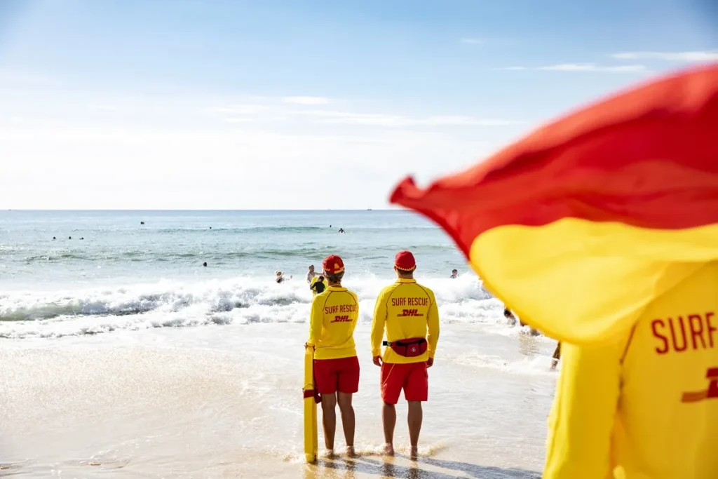 Two surf lifesavers watching swimmers beside a red and yellow flag on an Australian beach