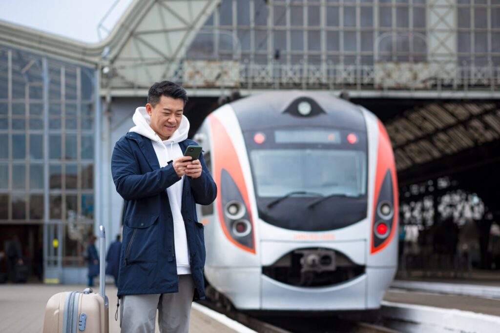 Traveller checking his smartphone on a railway platform with a modern passenger train behind him