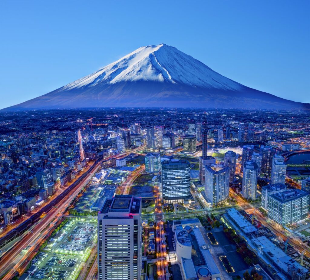 Snow-capped Mount Fuji above an illuminated cityscape at dusk in Japan