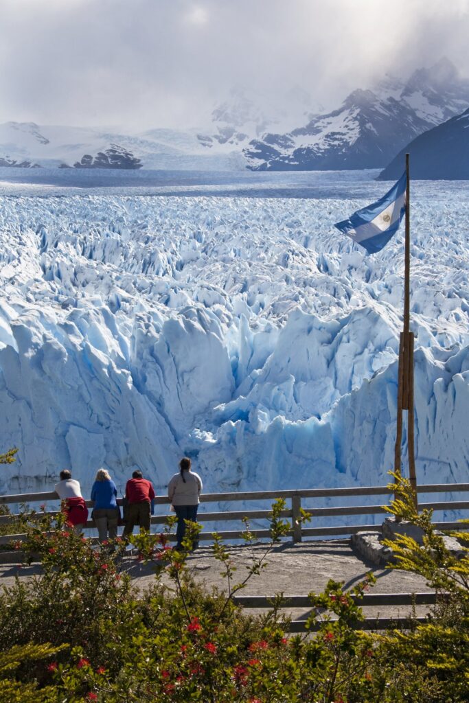 Visitors viewing Perito Moreno Glacier from a viewing platform beside an Argentine flag in Los Glaciares National Park, Patagonia