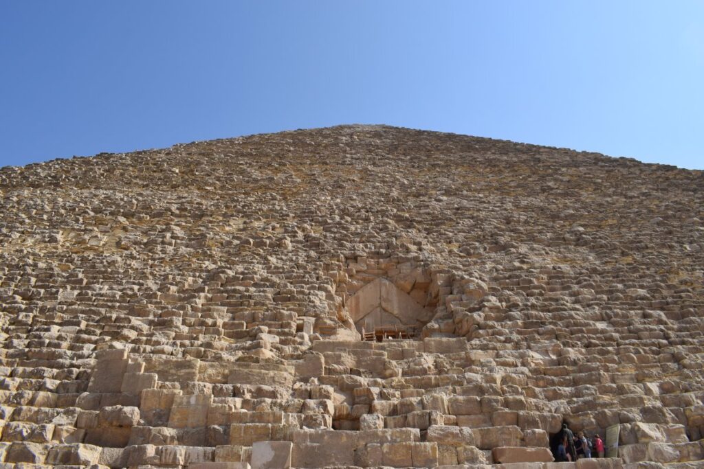 Close view of the Great Pyramid’s stone courses and entrance, with visitors at its base