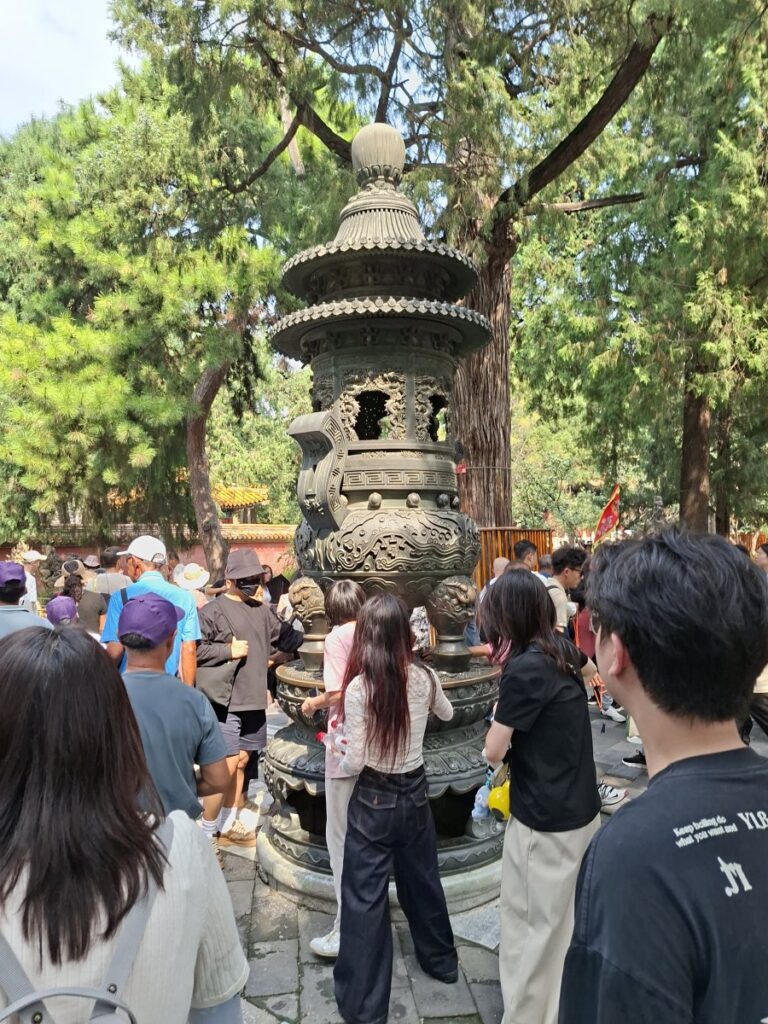 Visitors gather around an ornate ceremonial incense burner beneath the trees at the Forbidden City in Beijing