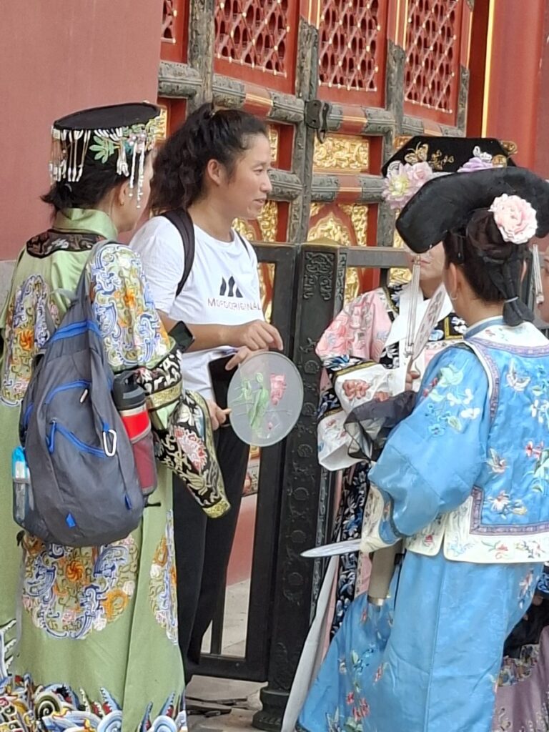 Visitors in colourful traditional-style clothing beside the red palace walls of the Forbidden City in Beijing