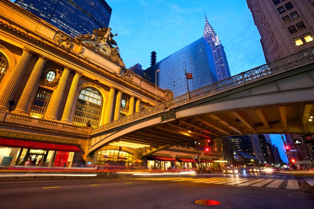 Illuminated Grand Central Terminal beside the Park Avenue Viaduct at dusk, with the Chrysler Building in the background