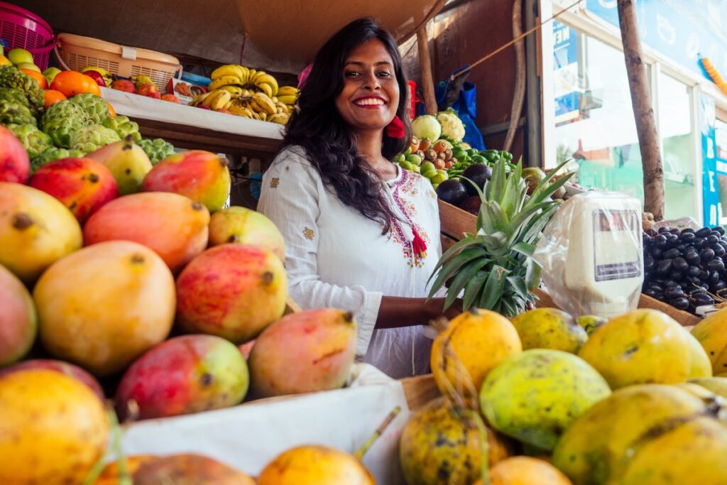 Woman standing among mangoes and other fresh fruit at a market stall