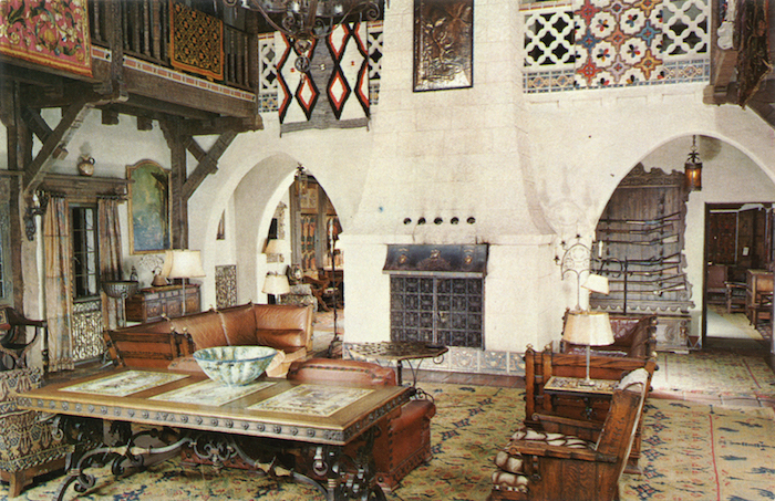 Historic interior of Scotty’s Castle, with arched doorways, decorative tiles, a wooden balcony and leather seating.