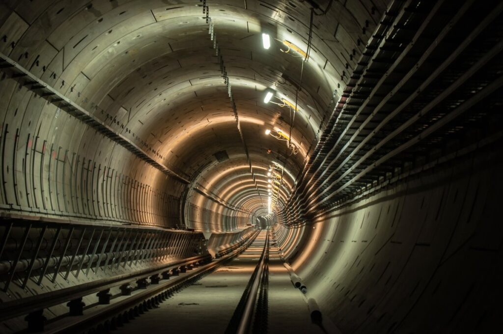 Railway tunnel interior with concrete lining, tracks, lighting and cables along the walls.