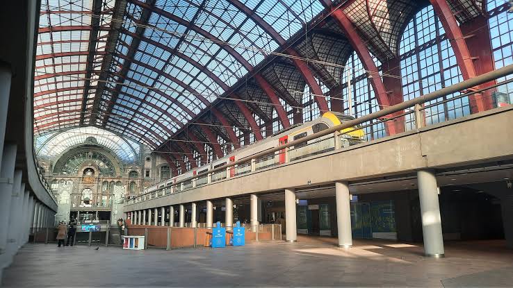 Train on an upper platform at Antwerp Central Station, beneath the arched steel and glass roof, with the concourse below.