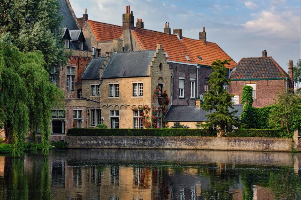 Historic canal-side houses in Bruges with stepped gables, red-tiled roofs and reflections in the water