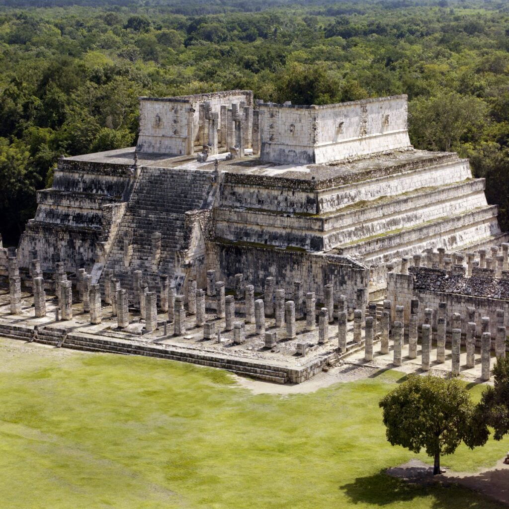 Temple of the Warriors at Chichén Itzá, Mexico, with stepped stone terraces and rows of columns surrounded by forest.