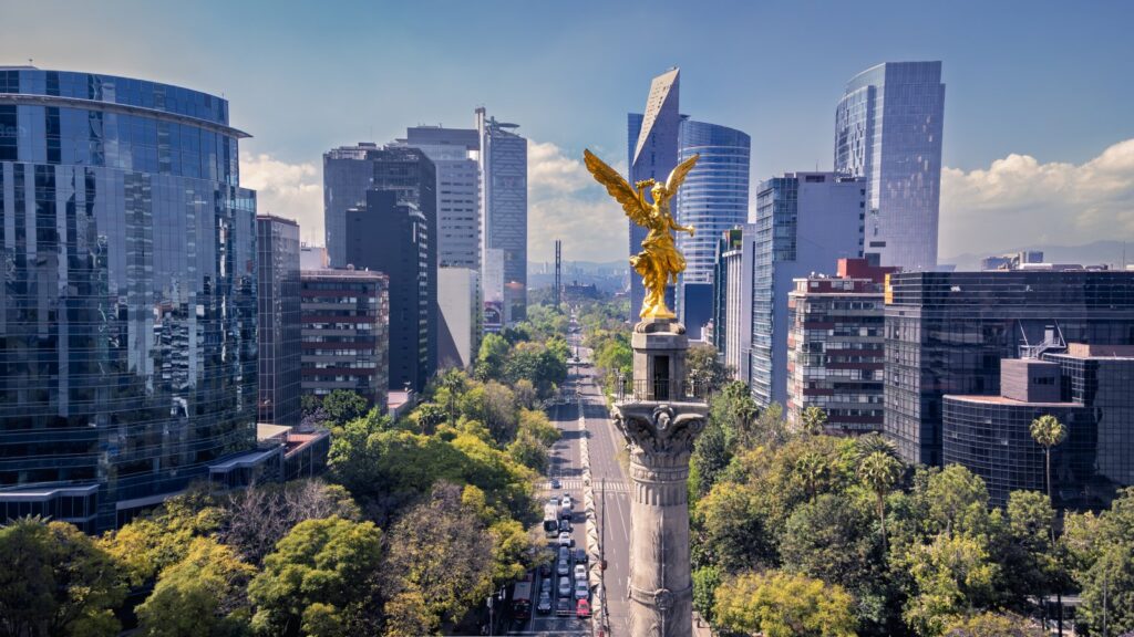 Angel of Independence monument on Paseo de la Reforma in Mexico City, Mexico, surrounded by modern skyscrapers and trees.