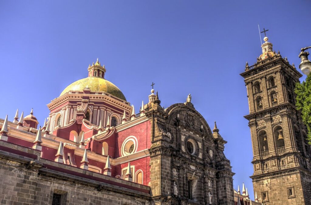 Historic church façade and ornate stone bell tower in Puebla, Mexico, beneath a clear blue sky.