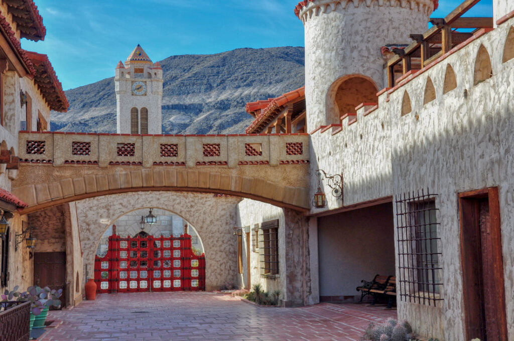 Courtyard at Scotty’s Castle, with an arched bridge, red gates and towers against the desert mountains of Death Valley.